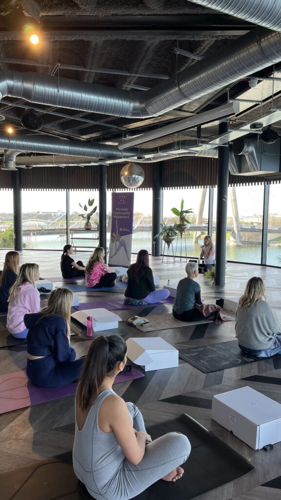 A group yoga session in a large open room with wall-to-ceiling windows and a waterfront view